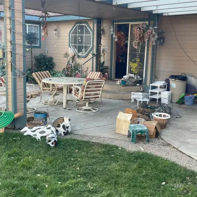 Sale Photo Thumbnail #49: Covered patio area featuring an outdoor dining set with striped cushions, decorative cow statues, plastic step stools, and assorted estate sale items.