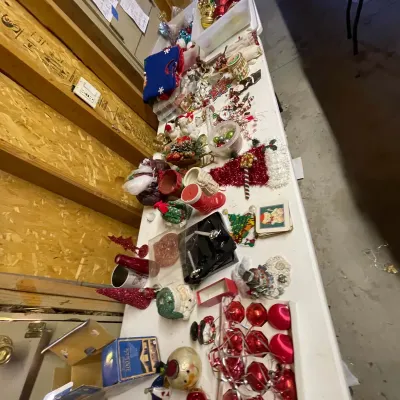 Sale Photo Thumbnail #8: Large collection of vintage and modern Christmas decorations, including red glass ball ornaments, figurines, stockings, tabletop trees, and holiday-themed decor displayed on a folding table.