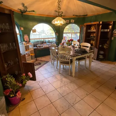 Sale Photo Thumbnail #93: Spacious dining room featuring a marble-top dining table with painted chairs, dark wood display cabinets filled with glassware, and large arched windows.