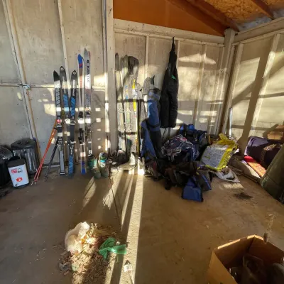 Sale Photo Thumbnail #35: Collection of vintage snow skis, poles, boots, ski bags, and winter sports gear arranged inside a storage shed or garage.