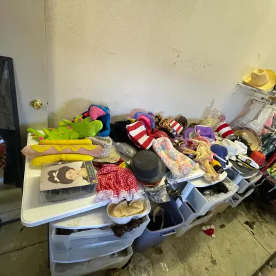 Sale Photo Thumbnail #13: Large assortment of costume accessories and hats, including novelties, wigs, top hats, and straw hats, displayed on a plastic folding table.
