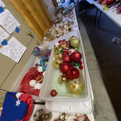 Sale Photo Thumbnail #9: Large collection of vintage and modern Christmas ornaments, including red and gold glittered baubles, organized in plastic bins along a sale table.