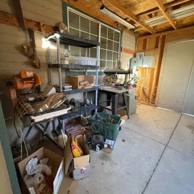 Sale Photo Thumbnail #52: Workshop area featuring various power tools, including a radial arm saw, tile saw, band saw, and multi-tier plastic shelving filled with supplies.