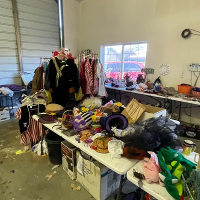 Sale Photo Thumbnail #12: Large collection of Halloween and dress-up costumes, hats, and novelty accessories arranged on folding tables and clothing racks in a garage setting.