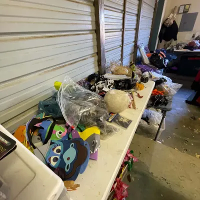 Sale Photo Thumbnail #19: Assorted costume masks, Halloween decorations, and novelty party items displayed on a folding table.