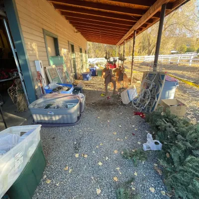 Sale Photo Thumbnail #41: Outdoor estate sale staging area under a covered walkway, featuring plastic storage totes, holiday decorations, and wooden lawn ornaments.