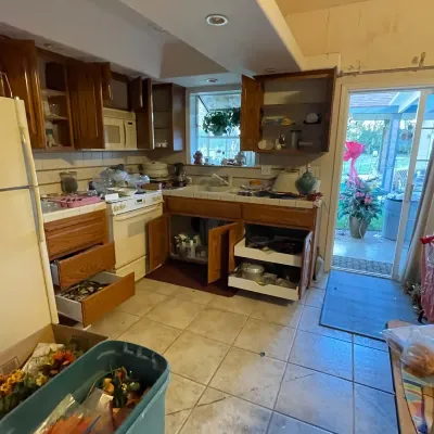 Sale Photo Thumbnail #46: Kitchen with oak cabinetry, tile countertops, a white electric range, and various cookware and household items stored inside drawers and cabinets.