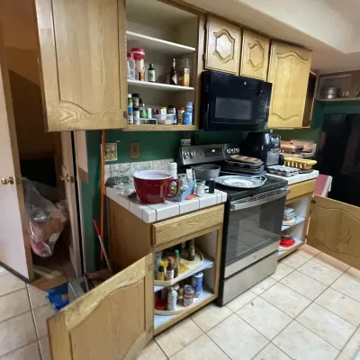 Sale Photo Thumbnail #61: Kitchen with oak cabinetry, tiled counter, black microwave, and stainless steel range, stocked with spices, baking pans, and small appliances.