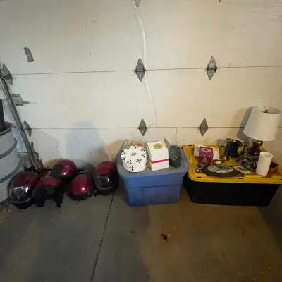 Sale Photo Thumbnail #73: Collection of red motorcycle helmets lined up next to storage totes filled with decorative home goods and a table lamp.