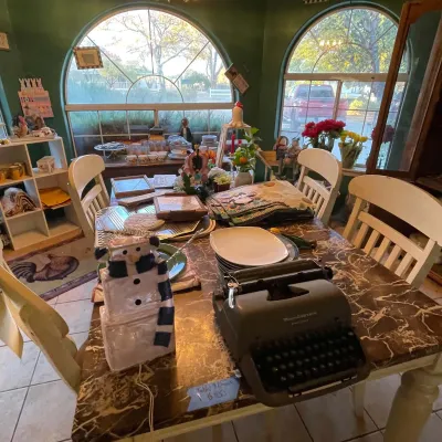 Sale Photo Thumbnail #99: Faux-marble top dining table with white chairs, filled with estate sale items including a vintage Remington manual typewriter, ceramic snowman, and dinnerware.
