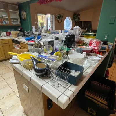 Sale Photo Thumbnail #62: Assorted kitchenware and household items displayed on a tiled island counter, including glassware, a yellow plastic colander, small appliances, and serving bowls.