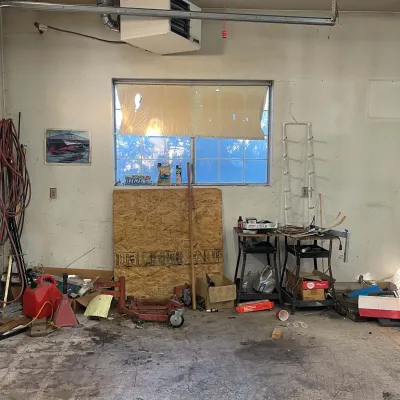 Sale Photo Thumbnail #60: Workshop garage interior containing a red engine stand, various tools, work tables, coiled hoses, and a wall-mounted heater unit.
