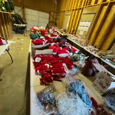 Sale Photo Thumbnail #3: Large collection of Christmas decorations arranged on folding tables, including red velvet bows, plush reindeer, Santa hats, and various craft supplies.