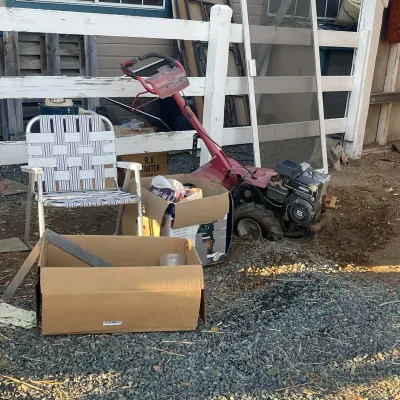 Sale Photo Thumbnail #32: Vintage red walk-behind garden tiller powered by a 5 HP Briggs & Stratton engine, shown alongside lawn chairs and various household items.