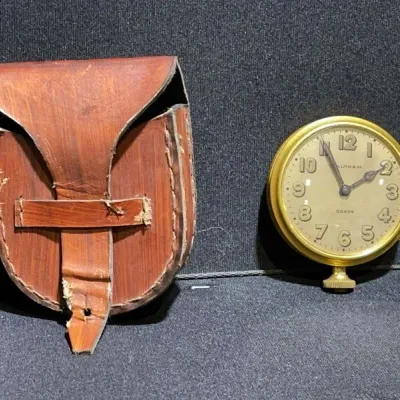 Sale Photo Thumbnail #17: Vintage Waltham 8-day brass automobile or pocket clock alongside a distressed stitched leather carrying pouch.
