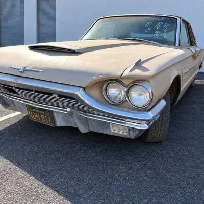 Sale Photo Thumbnail #3: Vintage mid-1960s Ford Thunderbird coupe in beige, featuring a front hood scoop, chrome grille and bumpers, dual headlights, and California black license plates.