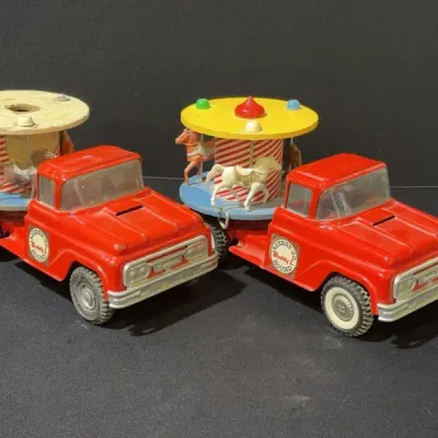 Sale Photo Thumbnail #22: Pair of vintage Buddy L red pressed-steel Merry-Go-Round pickup trucks featuring carousel horse attachments on the bed, showing light play wear.
