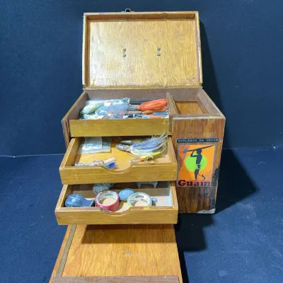 Sale Photo Thumbnail #83: Vintage wooden fishing tackle box featuring tiered drawers, side storage, and a Guam sticker, filled with assorted tackle, lures, and supplies.