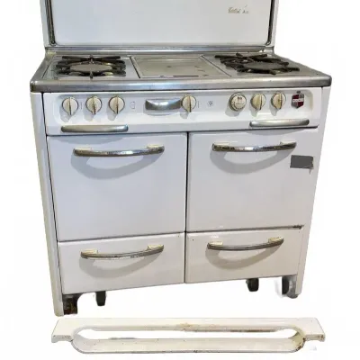 Sale Photo Thumbnail #31: Vintage Wedgewood white porcelain gas range with four burners, central griddle, folding splashguard back, and dual ovens, shown with detached bottom trim pieces.