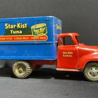 Sale Photo Thumbnail #21: Vintage pressed steel Star-Kist Tuna advertising delivery truck toy, featuring a red cab, blue cargo box with lithographed graphics, and minor paint wear throughout.