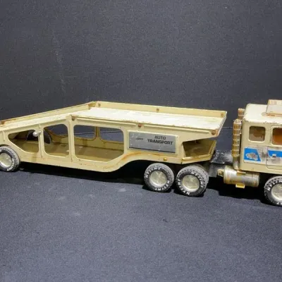 Sale Photo Thumbnail #91: Vintage Nylint press steel auto transport semi-truck toy, featuring an off-white cab and two-tier car carrier trailer with visible surface wear.