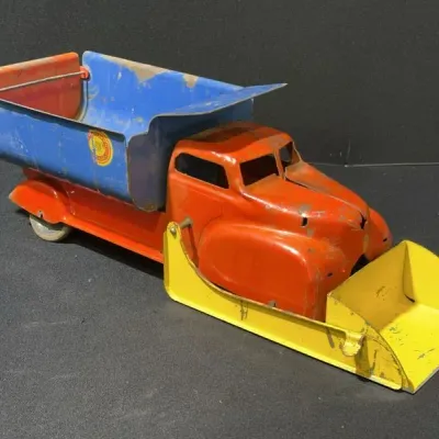 Sale Photo Thumbnail #72: Vintage pressed steel toy dump truck with front snowplow attachment, featuring primary blue, orange, and yellow paint with visible age-appropriate wear.
