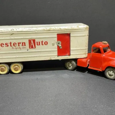 Sale Photo Thumbnail #73: Vintage pressed steel Western Auto semi-truck toy featuring a red cab and off-white trailer, showing moderate wear and paint loss.