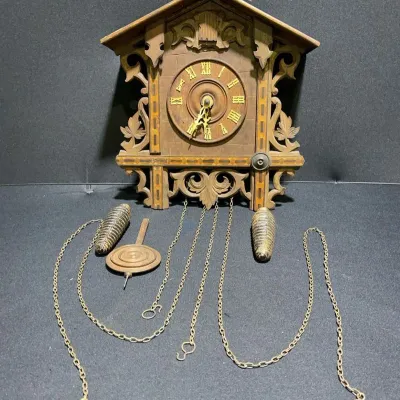 Sale Photo Thumbnail #49: Vintage carved wooden cuckoo clock featuring intricate scrollwork, inlaid border details, Roman numeral dial, pendulum, and dual pinecone weights.
