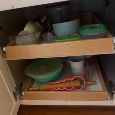 Sale Photo Thumbnail #8: Open kitchen cabinet featuring pull-out wooden drawers filled with assorted plastic food containers, mixing bowls, and kitchen utensils.