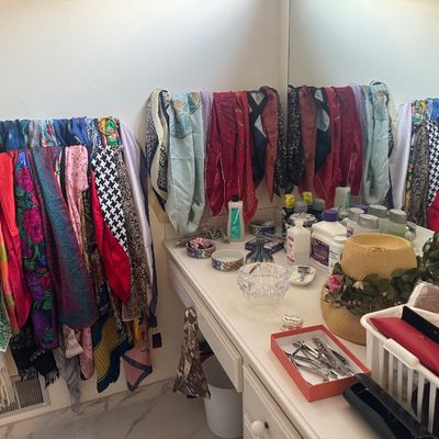 Sale Photo Thumbnail #52: A large collection of vintage colorful silk and fabric scarves draped over towel bars alongside a vanity filled with straw hats, toiletries, and small accessories.
