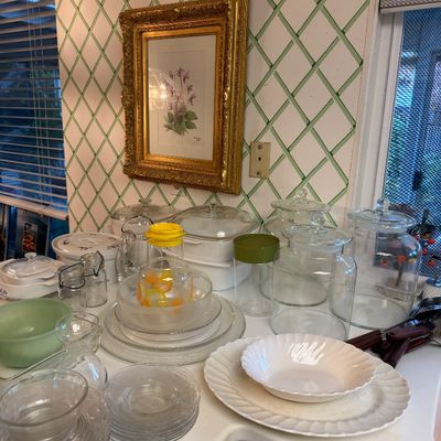 Sale Photo Thumbnail #24: Collection of vintage glassware, including clear glass storage jars, Pyrex cookware, and serving plates, arranged on a kitchen counter below a framed botanical print.