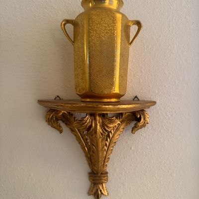 Sale Photo Thumbnail #16: Gold-toned porcelain urn with embossed floral patterns sitting atop a ornate carved wood-style wall sconce bracket.