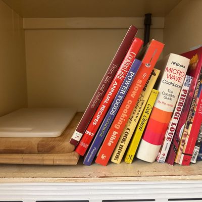 Sale Photo Thumbnail #30: A shelf stacked with vintage cookbooks and cutting boards, featuring titles like 'HP Books Microwave Cookbook' and 'The Slow Cooking Bible'.