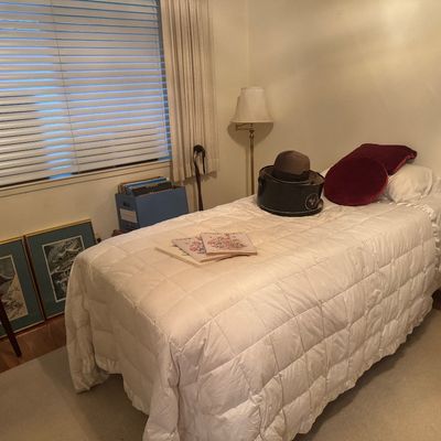 Sale Photo Thumbnail #62: Bedroom featuring a twin bed with a white quilted bedspread, a vintage fedora in its hat box, framed Asian art prints, vinyl records, and a floor lamp.