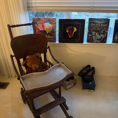 Sale Photo Thumbnail #55: Antique convertible wooden high chair with metal tray and plush teddy bear, set near coffee table books and footwear.