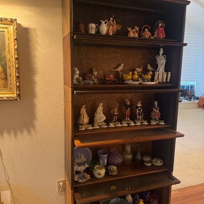 Sale Photo Thumbnail #9: Five-tier antique wooden barrister bookcase with glass lift doors, filled with various collectible figurines and ceramics.