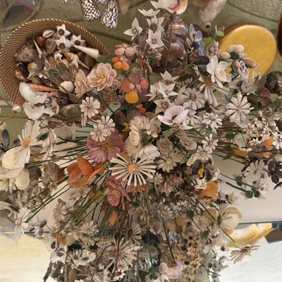 Sale Photo Thumbnail #15: Intricate bouquet of artificial flowers crafted from various sea shells, displayed alongside a woven basket filled with loose decorative shells.