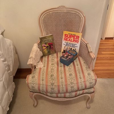 Sale Photo Thumbnail #65: French Provincial style armchair with cane back, whitewashed wood frame, and striped upholstery, holding a selection of books and a piece of lace.