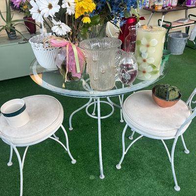 Sale Photo Thumbnail #103: White wrought iron bistro table with glass top and two matching chairs, displaying various decorative glass vases and floral arrangements.