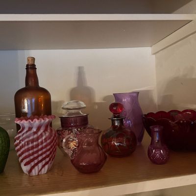 Sale Photo Thumbnail #43: Collection of vintage glass tableware and decorative bottles, including a pink and white swirl vase, ruby red scalloped bowl, green textured vase, and amber apothecary bottle.