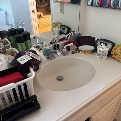 Sale Photo Thumbnail #56: Collection of bathroom vanity accessories and toiletries, including cosmetic bags, hair products, a floral ceramic jar, and a basket of hosiery.
