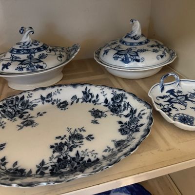 Sale Photo Thumbnail #34: Collection of blue and white ceramic tableware, including two covered tureen dishes, a scalloped dish with handle, and an oval serving platter with rose floral transferware design.