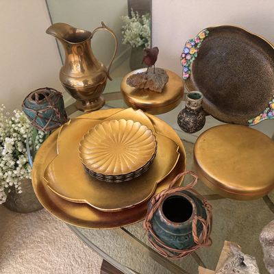 Sale Photo Thumbnail #20: Collection of decorative brass and metallic home accents, including stackable lotus-shaped trays, a brass pitcher, round trinket boxes, small ceramic vases, and a flower-trimmed dish.