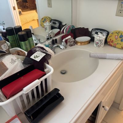 Sale Photo Thumbnail #51: Assorted bathroom accessories and personal care items arranged on a vanity counter, including cosmetic pouches, hairsprays, eyeglass cases, and a ceramic jar.