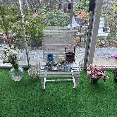 Sale Photo Thumbnail #97: White painted metal spring-base lawn chair holding a tray of abalone shells and decor, surrounded by artificial floral arrangements on green indoor-outdoor turf.