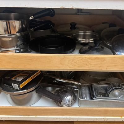 Sale Photo Thumbnail #27: Collection of kitchenware stored in pull-out cabinet drawers, including stainless steel pots, various lids, a Presto pressure cooker, baking pans, and small molds.