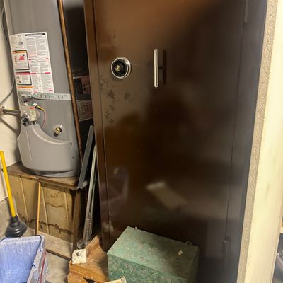 Sale Photo Thumbnail #76: Large brown floor safe featuring a combination dial and silver handle, situated alongside household items.