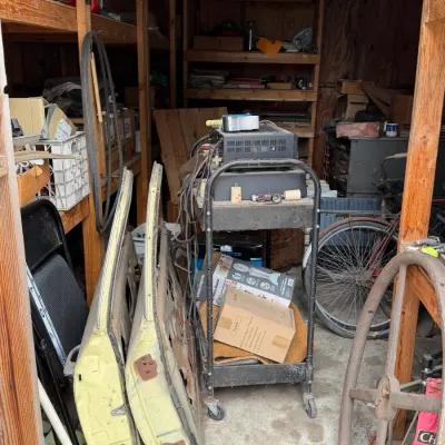 Sale Photo Thumbnail #29: A workshop shed packed with vintage items including yellow automobile doors, a rolling metal utility cart with electronics, a vintage bicycle, and various wooden shelving.