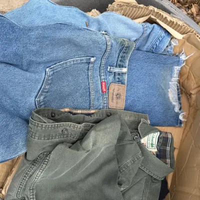 Sale Photo Thumbnail #27: Box of pre-owned men's workwear clothing, including Wrangler blue denim jeans and an L.L. Bean olive green flannel-lined shirt.