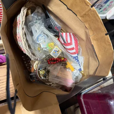 Sale Photo Thumbnail #26: Paper shopping bag filled with assorted small items, including costume jewelry, a woven basket, a small American flag, and novelty knick-knacks.